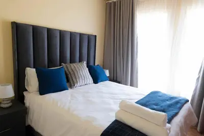 a bedroom with a large bed with blue pillows and a window at Pristine in Centurion