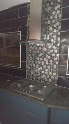 a kitchen counter with a stove and a tile wall at Budais guest lodge in Kempton Park