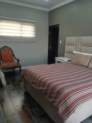 a bedroom with a bed and a chair and a window at Luxury Escape OR Tambo International in Kempton Park