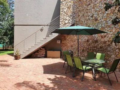 a table and chairs with an umbrella in front of a building at Cranes Nest Guest House in Pretoria