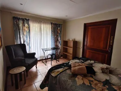 a bedroom with a bed and a chair and a table at Jolly Suites in Midrand