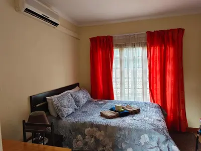 a bedroom with a bed with red curtains and a window at Jolly Suites in Midrand