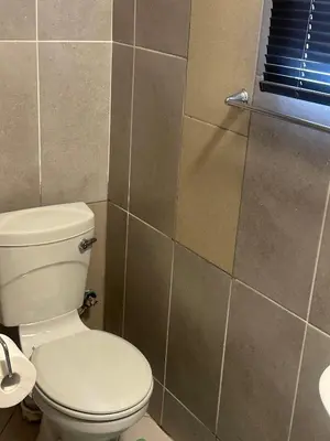 a bathroom with a white toilet and a tiled wall at Safaya Inn in Kempton Park
