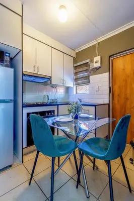 a kitchen with a glass table and two blue chairs at Meadow Lane in Johannesburg