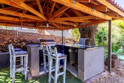 an outdoor kitchen with stools under a wooden roof at Meadow Lane in Johannesburg