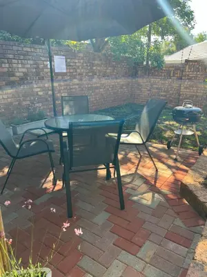 a table and chairs with an umbrella and a grill at Levinia Cottage in Pretoria