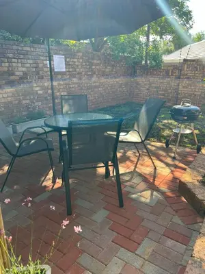 a table and chairs with an umbrella and a grill at Levinia Cottage in Pretoria