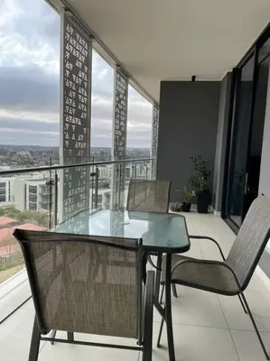a glass table and chairs on a balcony with a view at Your Oasis in Waterfall City in Midrand