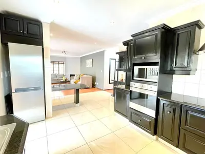 a kitchen with black cabinets and a living room at BB Hers Cheesy in Midrand