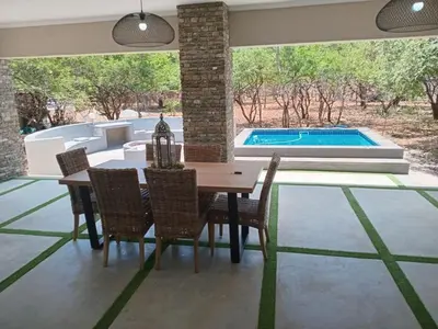 a dining room with a table and chairs and a swimming pool at Taíta Lodge in Marloth Park