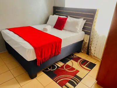 a bedroom with a bed with a red blanket on it at KINGs' PALACE GUESTHOUSE in Ermelo