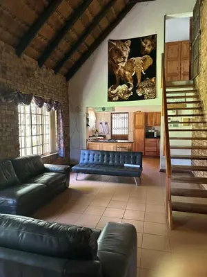 a living room with black leather couches and a staircase at Okgethilwe Lodge in Sabie