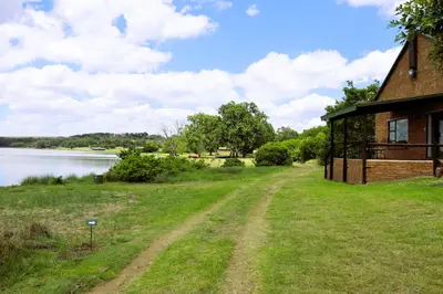 a house with a dirt road next to a body of water at Meerrus Self-Catering Home in Lake Chrissie