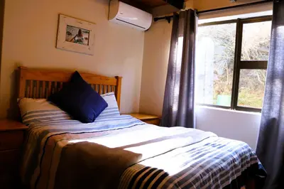 a bed with a blue pillow sitting next to a window at Meerrus Self-Catering Home in Lake Chrissie