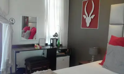 a bedroom with a bed and a desk with a mirror at Cu Guest House in Phalaborwa