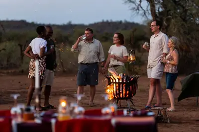 a group of people standing around a fire at Pafuri Camp by RETURN Africa in Makuleke Contract Park