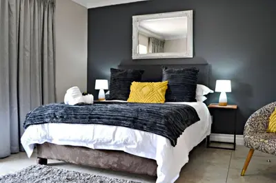 a bedroom with a bed with yellow pillows and a mirror at Bokmakierie Gastehuis Emalahleni Pty Ltd in Witbank
