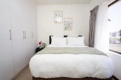 a white bedroom with a large bed and a window at Mercy land Apartment 1 in Midrand