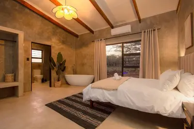 a bedroom with a large bed and a bath tub at Pillows Luxury Safari Villa, Wood-Fired Hottub, Giraffe-Feeding-Tower, Large Private Pool in Marloth Park