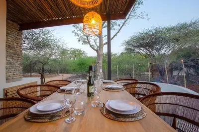 a wooden table with plates and wine glasses on it at Pillows Luxury Safari Villa, Wood-Fired Hottub, Giraffe-Feeding-Tower, Large Private Pool in Marloth Park