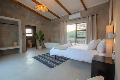 a bedroom with a large bed and a bath tub at Pillows Luxury Safari Villa, Wood-Fired Hottub, Giraffe-Feeding-Tower, Large Private Pool in Marloth Park