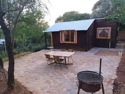 a small wooden cabin with a table and chairs at Koinonia Bush Lodge in Hartbeespoort