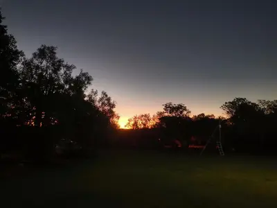 a sunset in a field with trees and a swing at Hartbeespoort Cara-glamping self-cater units in Pretoria