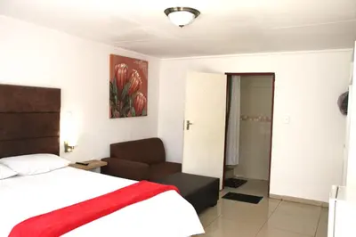 a bedroom with a bed and a couch and a painting at Royal Chestnut Guesthouse in Kempton Park