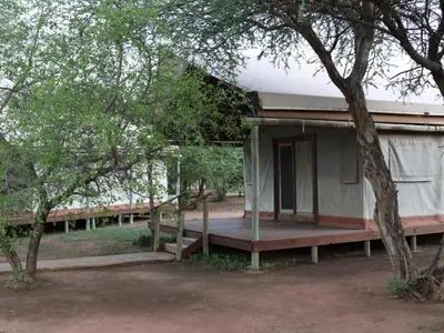 a small building with a porch and a tree at Ngata Safari Lodge in Hammanskraal