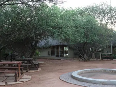 a building with picnic tables and trees in front of it at Ngata Safari Lodge in Hammanskraal