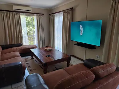a living room with leather furniture and a flat screen tv at The Green Lizard Self-catering House in Nelspruit