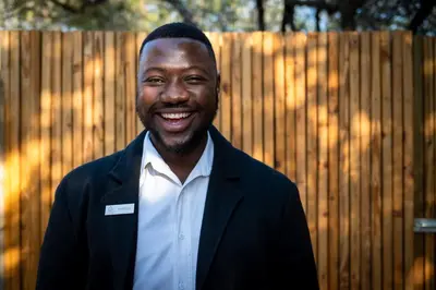 a man in a suit smiling in front of a fence at Khiwane Boutique Hotel in Hoedspruit