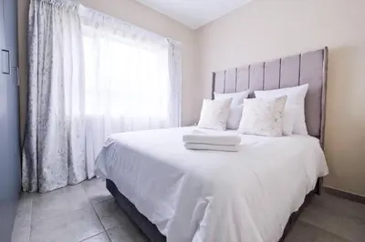 a bedroom with a bed with white sheets and a window at Diamond Hill in Midrand