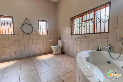 a bathroom with a tub and a toilet and windows at The Orange Tree Guest House in Nelspruit
