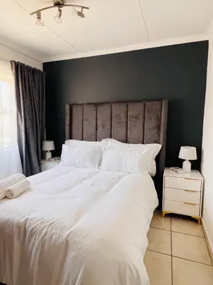 a bedroom with a white bed with a gray wall at The Lux apartment in Polokwane