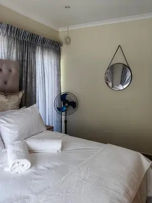 a bedroom with a white bed with a lamp and a mirror at The Crown in Nelspruit