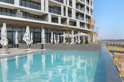 a swimming pool in front of a building with umbrellas at Chic & Elegant at Ellipse in Midrand