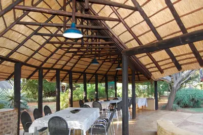 a group of tables and chairs under a wooden roof at Gallery Inn in Bela-Bela