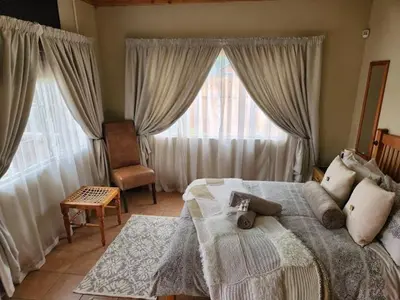 a bedroom with a bed and a chair and windows at Tranquility Guest House in Sabie