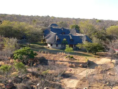 a blue house with a thatched roof in a field at Izintaba Private Game Reserve Waterberg in Vaalwater
