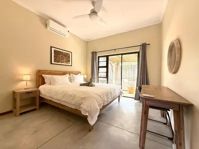 a bedroom with a bed and a table and a window at Plumtree House in Hoedspruit