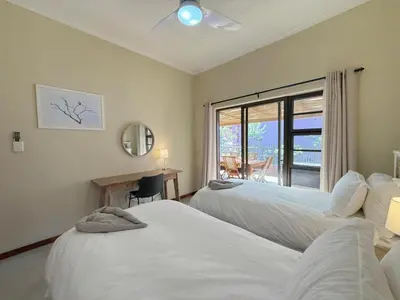 a bedroom with two beds and a desk and a window at Plumtree House in Hoedspruit