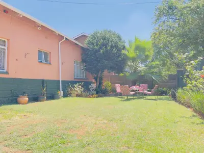 a yard with a pink house with a table and chairs at Urban Oasis Guest House in Pretoria