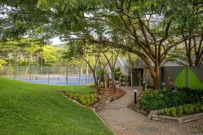 a park with a tree and a tennis court at First Group Sanbonani Resort in Hazyview