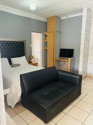 a bedroom with a bed and a black leather couch at Northgatelodges and Tours in Polokwane
