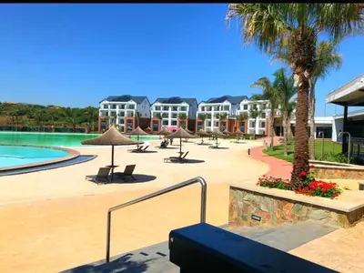 a resort with a pool and palm trees and a hotel at The blyde apartment in Pretoria