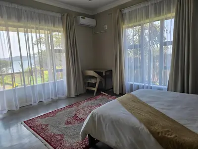 a bedroom with a bed and large windows and a desk at Muca House in Thohoyandou