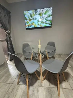a dining room table with four chairs and a television on a wall at Nettle Nest Accommodation in Polokwane
