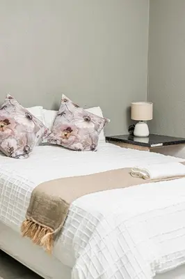 a white bed with pink pillows and a table with a lamp at Mahlakwena Crown Crest in Steelpoort