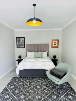 a bedroom with a large bed and a chair at Nelspruit Modern Apartment #2 - Self Check-In in Nelspruit